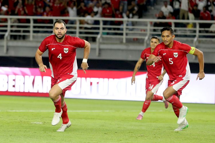 Rizky Ridho mengenakan ban kapten kuning di lengan kirinya saat berlari di lapangan bersama Jordi Amat dalam pertandingan Timnas Indonesia.