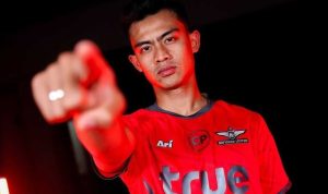 Pemain sepak bola Timnas Indonesia, Pratama Arhan, berpose menunjuk ke arah kamera sambil mengenakan jersey merah resmi Bangkok United FC.