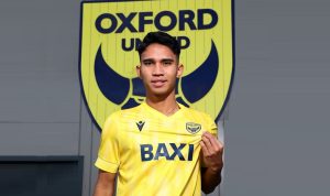 Marselino Ferdinan mengenakan jersi kuning dengan latar belakang logo klub Oxford United