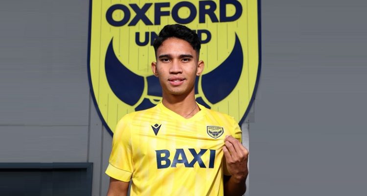 Marselino Ferdinan mengenakan jersi kuning dengan latar belakang logo klub Oxford United