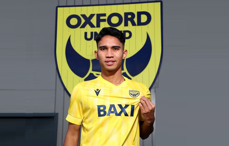 Marselino Ferdinan mengenakan jersi kuning dengan latar belakang logo klub Oxford United