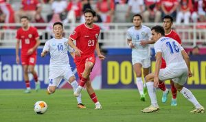 Nathan Tjoe-A-On dengan jersey merah nomor 23 menggiring bola saat membela Timnas Indonesia melawan tim lawan berjersey putih.