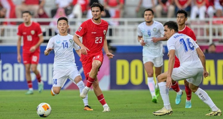 Nathan Tjoe-A-On dengan jersey merah nomor 23 menggiring bola saat membela Timnas Indonesia melawan tim lawan berjersey putih.