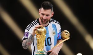 lionel-messi-pensiun-setelah-piala-dunia-2026.webp Lionel Messi tersenyum sambil memegang trofi Piala Dunia dan penghargaan Golden Ball mengenakan jersey timnas Argentina.