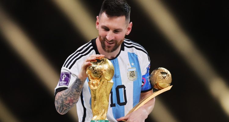 lionel-messi-pensiun-setelah-piala-dunia-2026.webp Lionel Messi tersenyum sambil memegang trofi Piala Dunia dan penghargaan Golden Ball mengenakan jersey timnas Argentina.