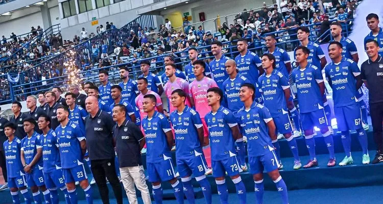 persib-bandung-bidik-pemain-asing-baru.webp Skuat lengkap Persib Bandung berfoto bersama mengenakan jersey biru di tepi lapangan sebelum pertandingan dimulai.