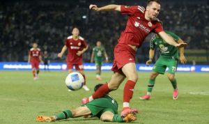 Pemain Persebaya berjersey hijau melakukan sliding tackle menghalau bola dari pemain Persija.