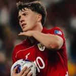 ole-romeny-pemain-timnas-indonesia.webp Striker Ole Romeny mengenakan jersey merah Timnas Indonesia berlambang Garuda sambil memegang bola di lapangan.