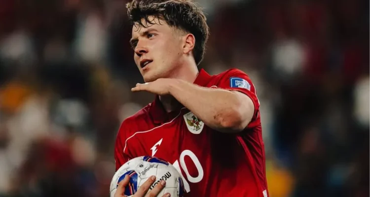 ole-romeny-pemain-timnas-indonesia.webp Striker Ole Romeny mengenakan jersey merah Timnas Indonesia berlambang Garuda sambil memegang bola di lapangan.