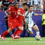 Lionel Messi dengan seragam timnas Argentina sedang menggiring bola dengan lincah melewati hadangan dua pemain lawan di lapangan hijau.