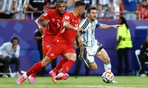 Lionel Messi dengan seragam timnas Argentina sedang menggiring bola dengan lincah melewati hadangan dua pemain lawan di lapangan hijau.