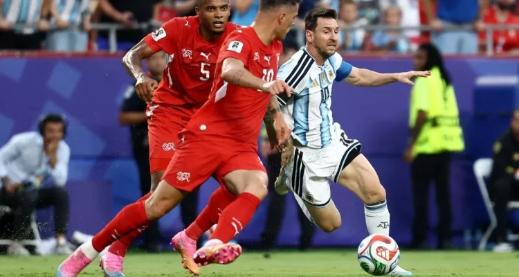 aksi-lionel-messi-giring-bola-timnas-argentina.webp Lionel Messi dengan seragam timnas Argentina sedang menggiring bola dengan lincah melewati hadangan dua pemain lawan di lapangan hijau.