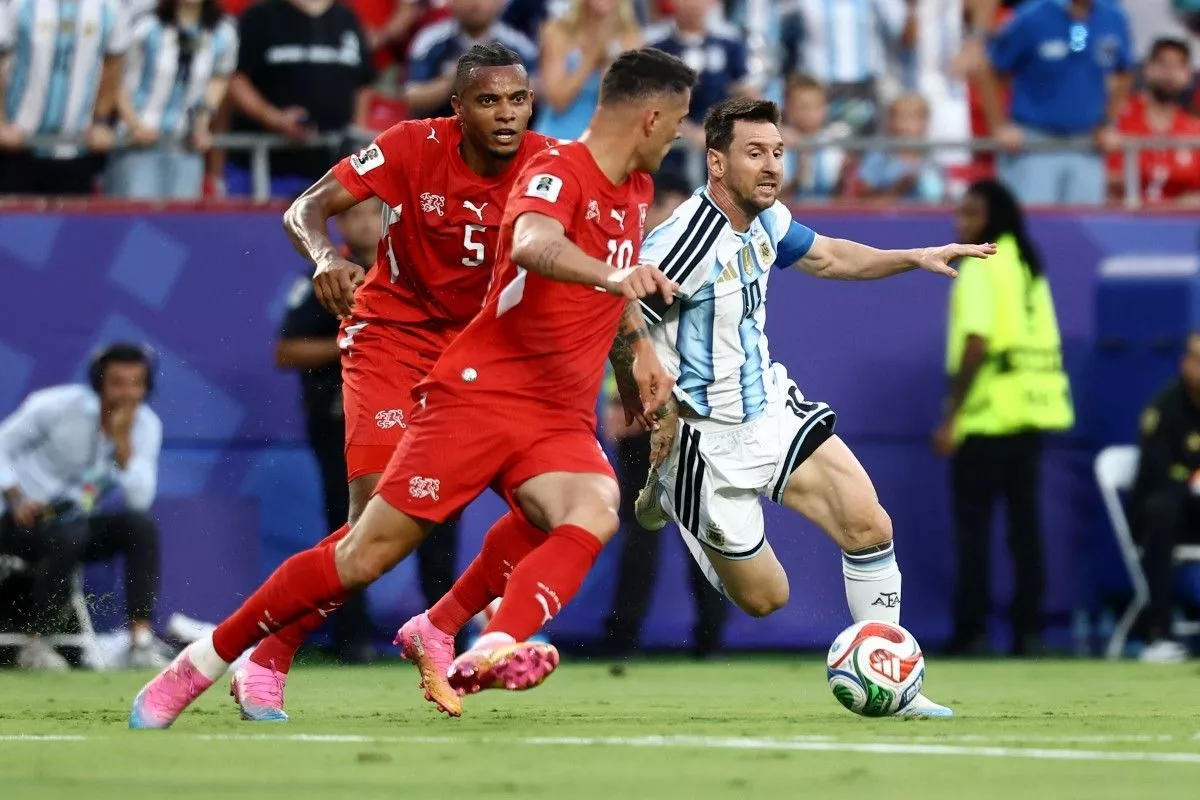 Lionel Messi dengan seragam timnas Argentina sedang menggiring bola dengan lincah melewati hadangan dua pemain lawan di lapangan hijau.