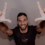 denis-kolinger-bek-baru-persija-jakarta.webp Denis Kolinger, bek asing baru Persija Jakarta asal Jerman-Kroasia, tersenyum ke arah kamera sambil membentuk simbol "L" (The Jakmania) dengan kedua tangannya.