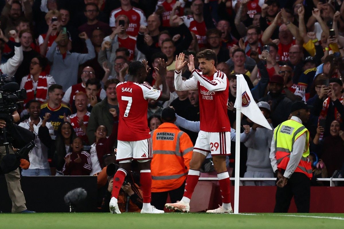 Pemain Arsenal Bukayo Saka dan Kai Havertz melakukan selebrasi high five di sudut lapangan di hadapan para pendukung.