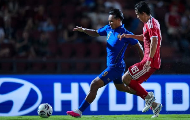 Striker Timnas Thailand, Teerasil Dangda (No. 9), berusaha melewati hadangan bek Singapura dalam pertandingan semifinal leg kedua Piala AFF 2026. Meski kalah tipis, Thailand berhasil mengunci tiket ke final berkat keunggulan agregat gol.