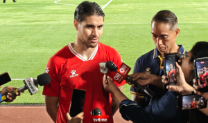 kevin-diks-kapten-timnas-indonesia-asean-cup-2026.webp Kevin Diks mengenakan jersi merah Timnas Indonesia saat diwawancarai oleh para wartawan di pinggir lapangan.