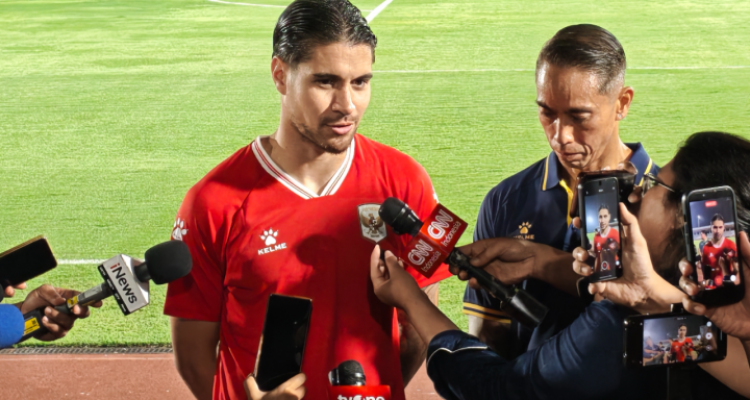 kevin-diks-kapten-timnas-indonesia-asean-cup-2026.webp Kevin Diks mengenakan jersi merah Timnas Indonesia saat diwawancarai oleh para wartawan di pinggir lapangan.