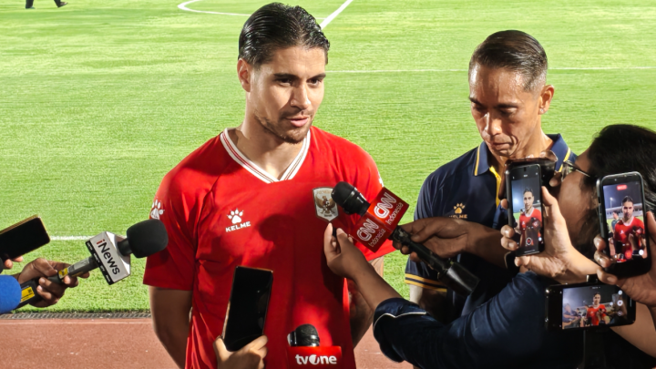 Kevin Diks mengenakan jersi merah Timnas Indonesia saat diwawancarai oleh para wartawan di pinggir lapangan.