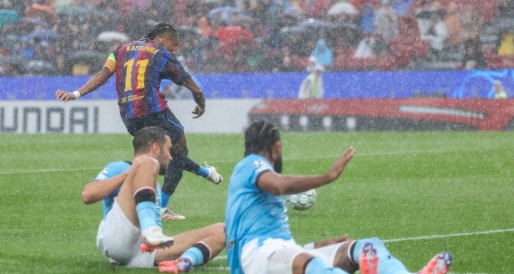 barcelona-vs-feyenoord-raphinha-tendangan.webp Raphinha pemain Barcelona melesakkan tendangan keras ke arah gawang Feyenoord di tengah hujan deras.