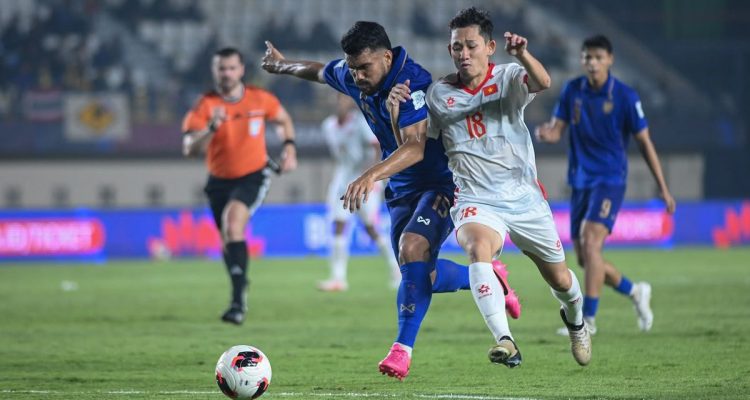 timnas-thailand-vs-vietnam-fifa-asean-cup.webp Pemain Timnas Thailand jersey biru berebut bola sengit dengan pemain Vietnam jersey putih di FIFA ASEAN Cup.
