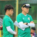 shin-tae-yong-bersama-asisten-pelatih-timnas.webp Pelatih Shin Tae-yong mengenakan topi hitam dan baju hijau sedang bersedekap mengamati sesi latihan Timnas.
