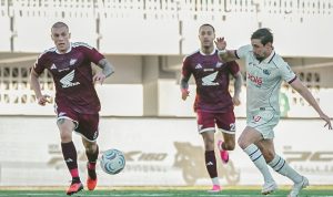 Pemain PSM Makassar berjersey merah marun menguasai bola di bawah tekanan pemain Arema FC.