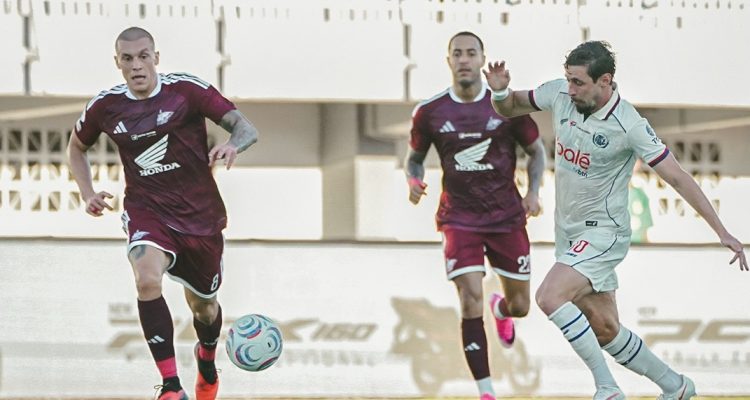 Pemain PSM Makassar berjersey merah marun menguasai bola di bawah tekanan pemain Arema FC.