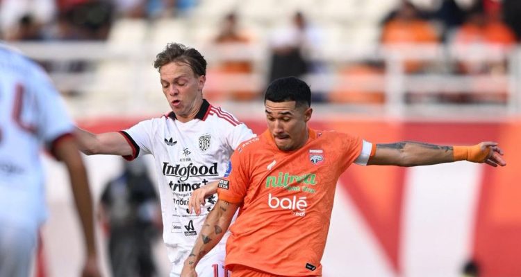 borneo-fc-vs-bali-united-menang-di-samarinda.webp Pemain Borneo FC berjersey oranye berebut bola dengan pemain Bali United berjersey putih di lapangan.