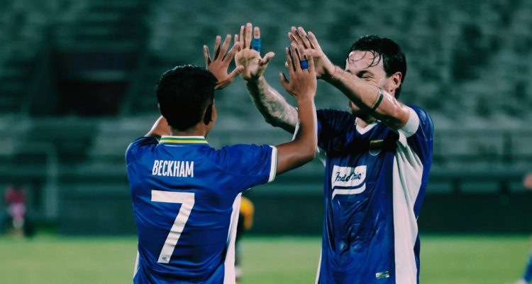 persib-bandung-vs-psm-kedalaman-skuad-maung-bandung.webp Dua pemain Persib Bandung, Beckham Putra bernomor punggung 7 dan rekannya, melakukan selebrasi tos tangan bersama di lapangan.