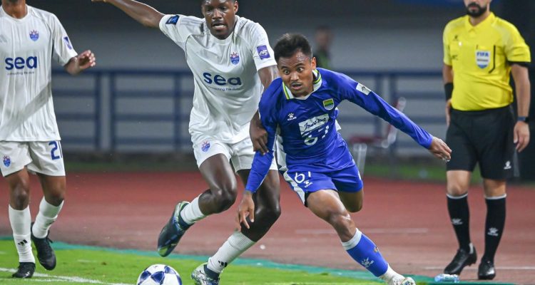 saddil-ramdani-tinggalkan-persib-persebaya.webp Saddil Ramdani menggunakan jersey biru saat menggiring bola di bawah tekanan pemain lawan di lapangan hijau.