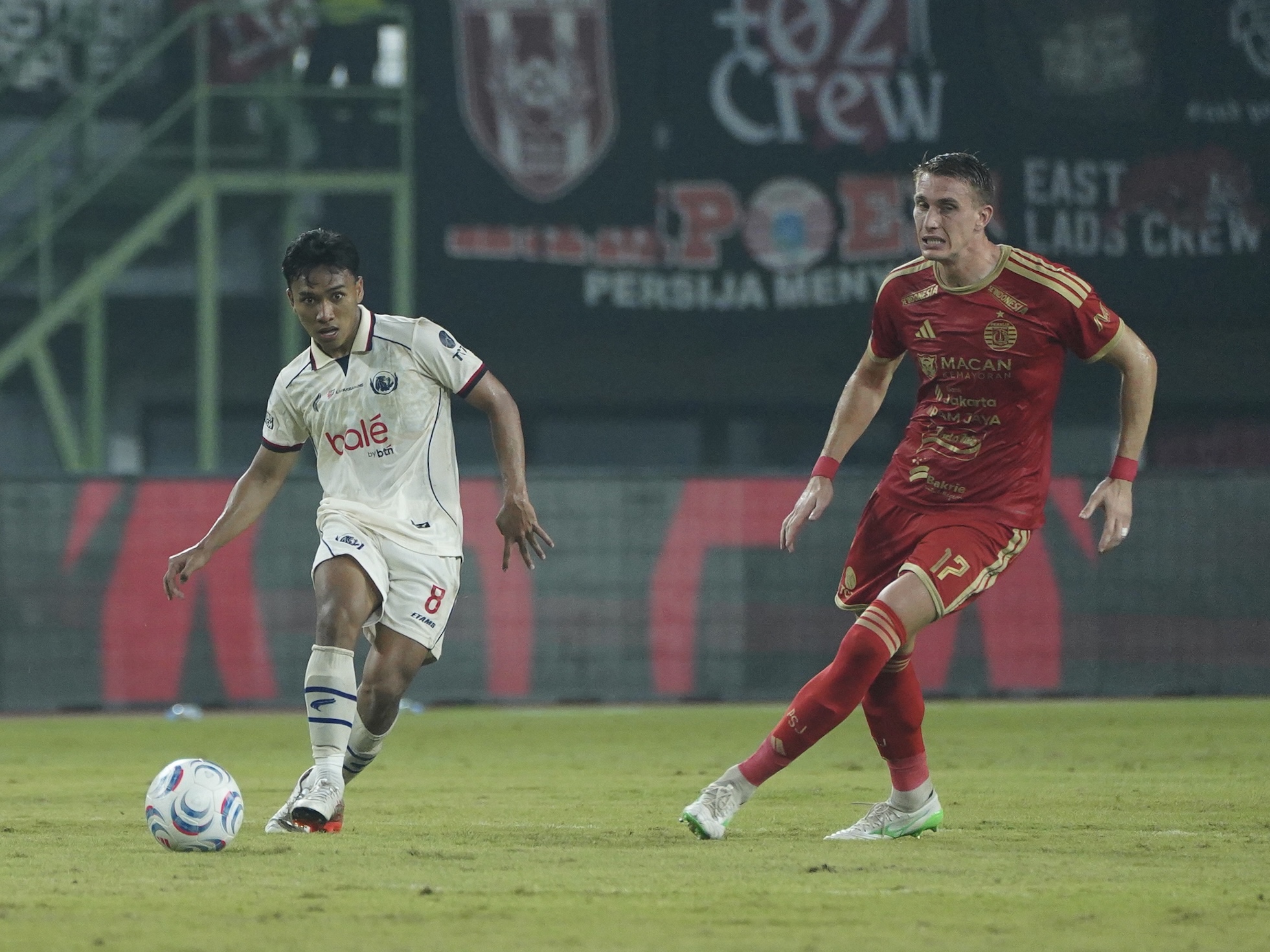Pemain Persija Jakarta bernomor punggung 17 membendung pergerakan pemain Arema FC di lapangan hijau.