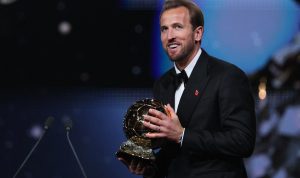 ballon-dor-2026-milik-harry-kane-penantang-lain-gigit-jari-7.webp Harry Kane tersenyum bangga sambil memegang trofi Ballon d'Or 2026 di atas panggung penghargaan.