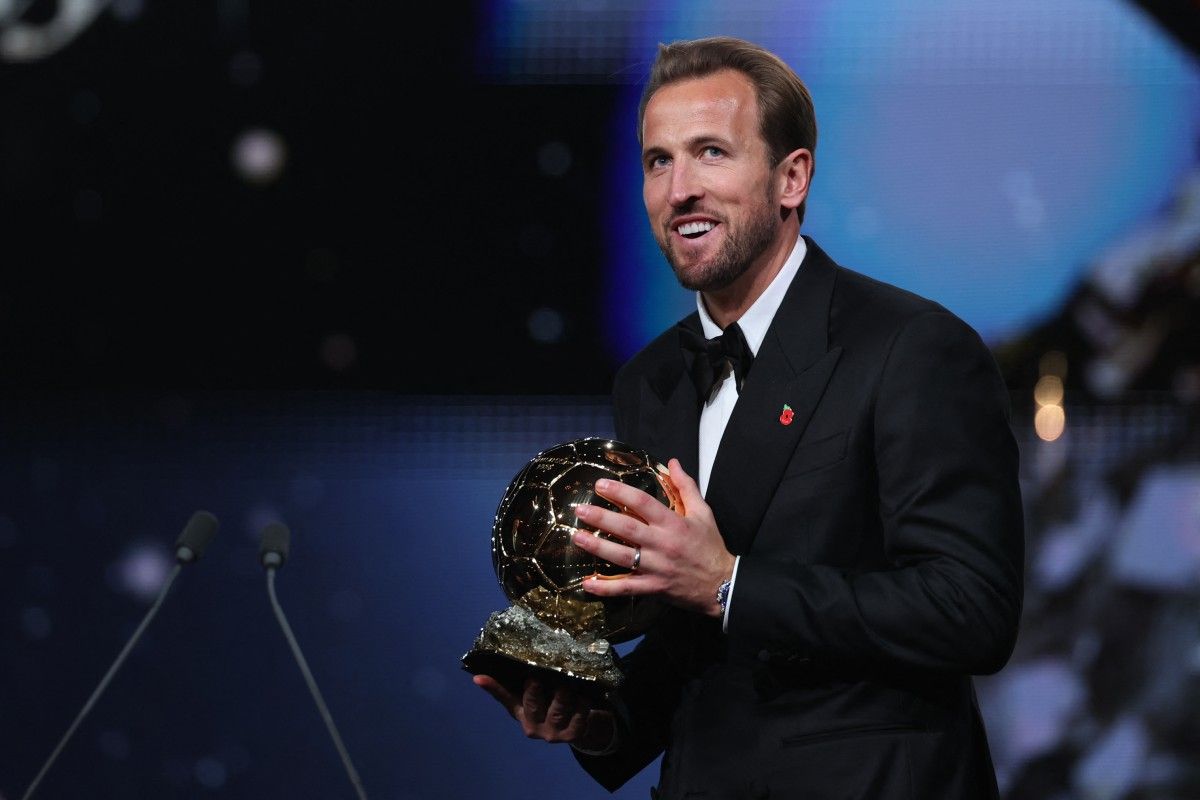 Harry Kane tersenyum bangga sambil memegang trofi Ballon d'Or 2026 di atas panggung penghargaan.